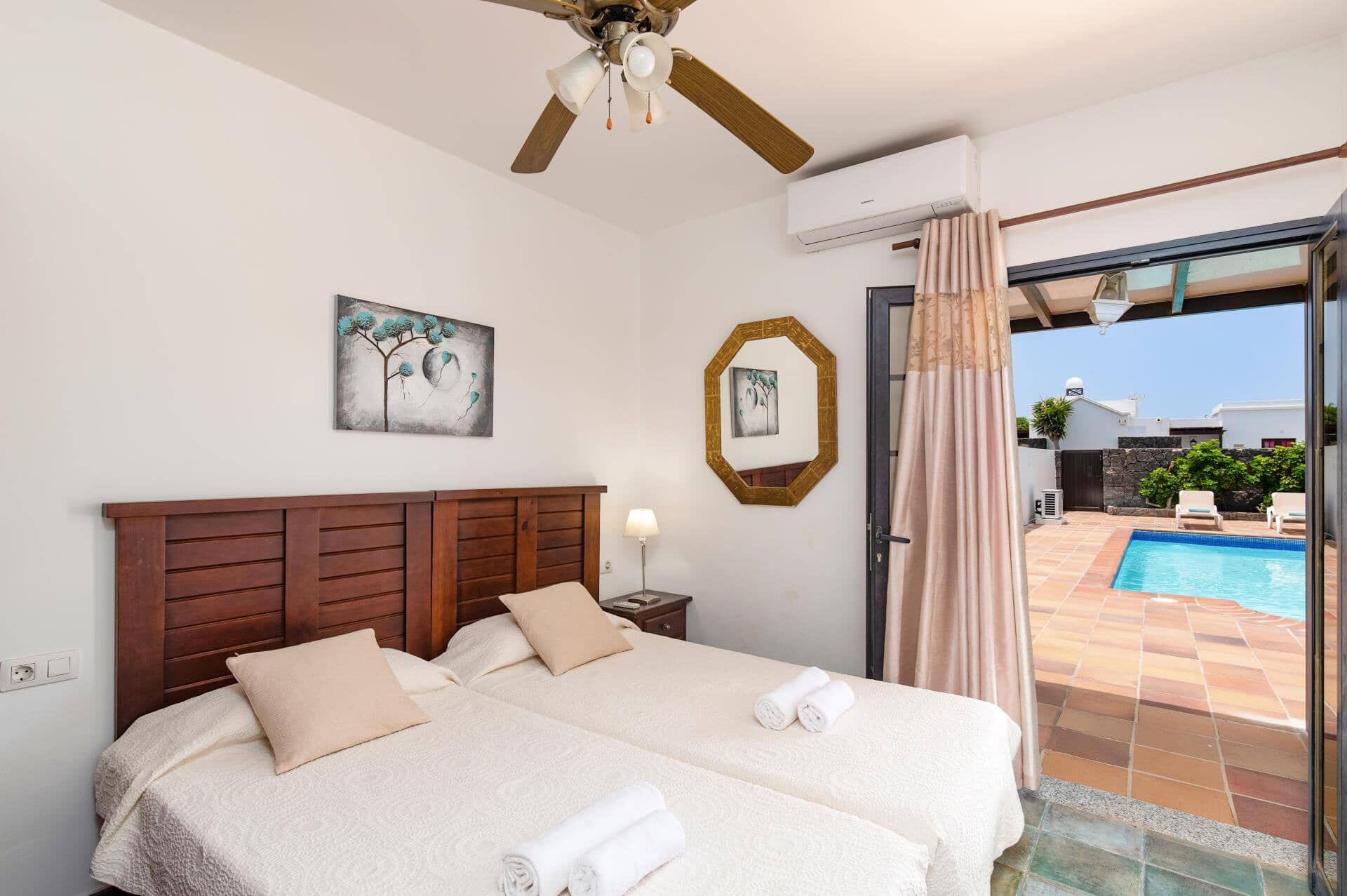 A hotel room with a large bed, a ceiling fan, a painting, and a view of a swimming pool.