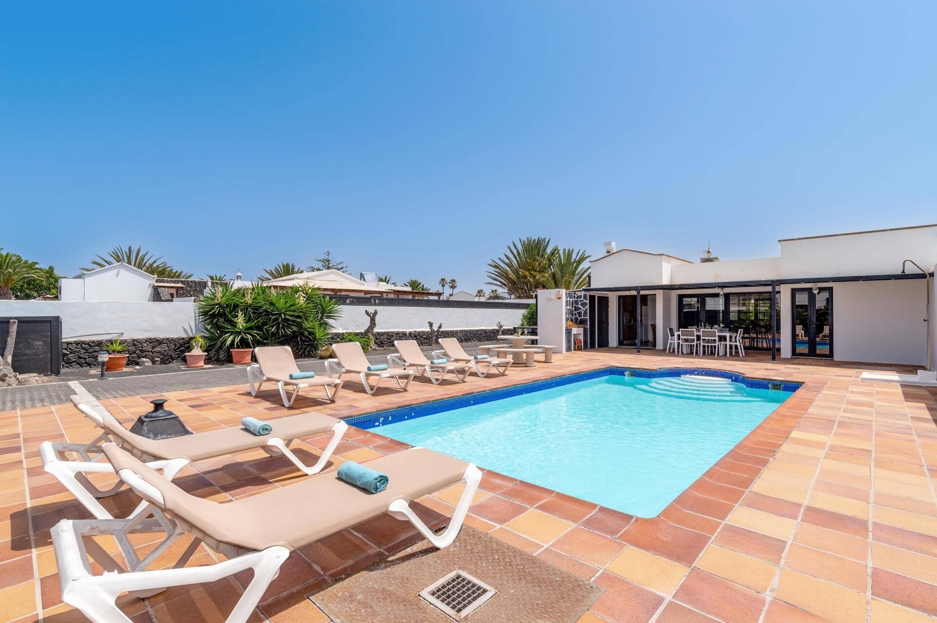 A rooftop pool area with lounge chairs, a dining table, and a covered seating area.