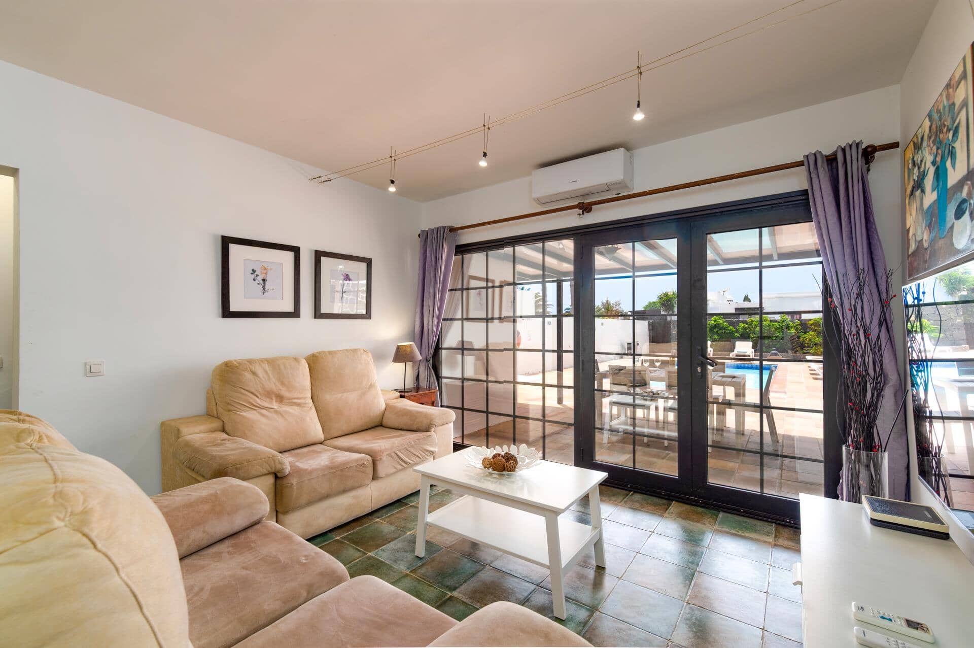 Un salon avec un canapé beige, une table basse blanche et une grande porte-fenêtre coulissante donnant sur un espace extérieur avec une piscine.