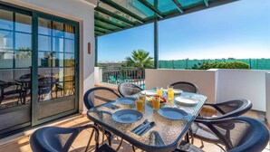 Un coin repas avec une table dressée pour deux personnes, une cloison en verre et une vue sur une piscine et la verdure.