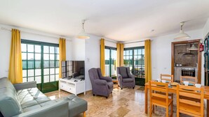 Un salon moderne comprenant un canapé, deux fauteuils, un téléviseur et un coin repas avec une table et des chaises.