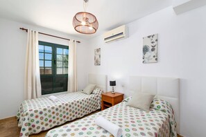 Una stanza con due letti, una finestra con tende, un lampadario e un condizionatore d'aria, più elementi decorativi alle pareti.
