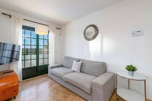 A modern living room with a sofa, a TV, a small table with a plant, and a large window with curtains.