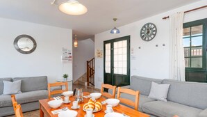 Ein Essbereich mit einem Holztisch, gedeckt für das Frühstück, zwei grauen Sofas, einer Uhr und einer Tür mit grünem Rahmen.