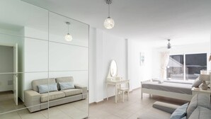 A modern living room with a sofa, a glass partition, a desk with a mirror, and a bed.