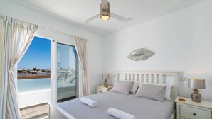 A bedroom with a bed, nightstands, a ceiling fan, a view through a glass door, and a decorative wall piece.