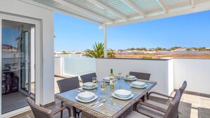 A covered outdoor dining area with a table set for four, overlooking a landscape with buildings and greenery.
