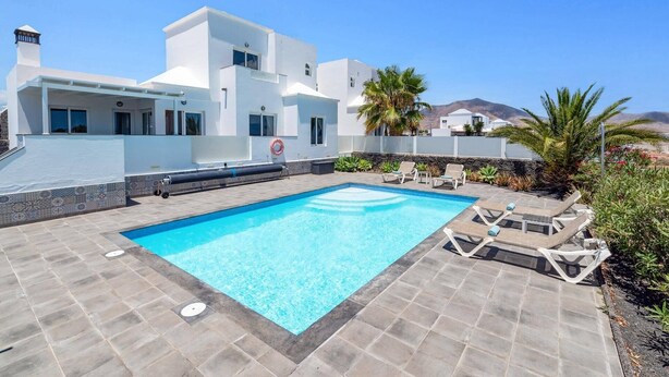 A modern white building with a swimming pool and lounge chairs.