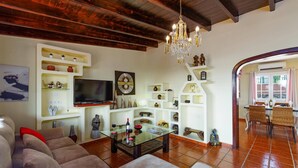 Una sala de estar con un sofá, televisor, estantes decorativos y una araña.