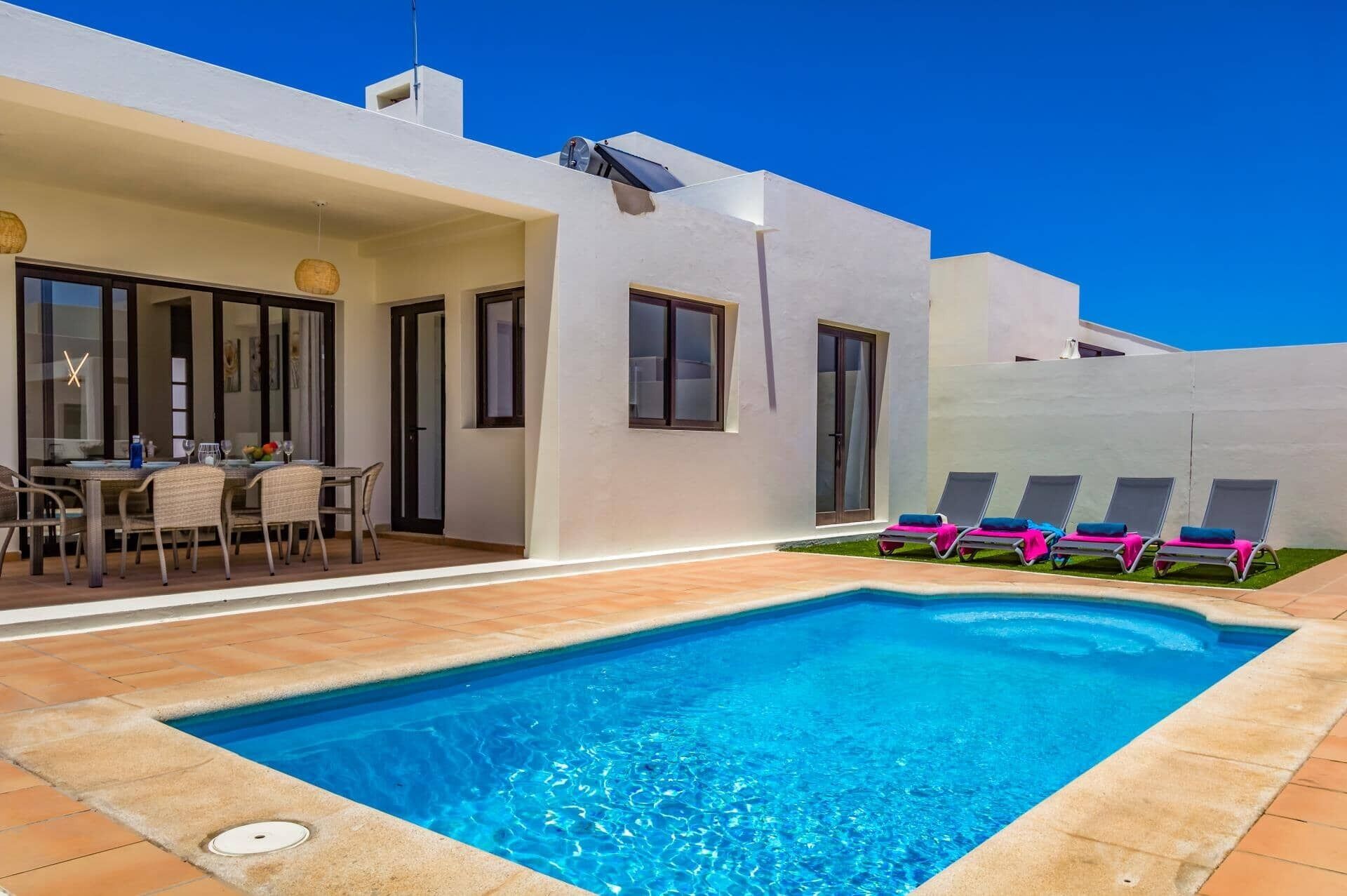 A modern house with a swimming pool, a dining area, and a patio with lounge chairs.