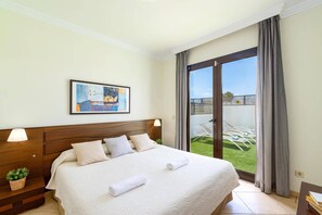 Une chambre d’hôtel avec un grand lit, un tableau au mur et une vue sur une pelouse verdoyante, visible à travers la porte-fenêtre.