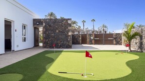 Een golfbaan met een vlag op hole 3, een stenen muur en palmbomen.