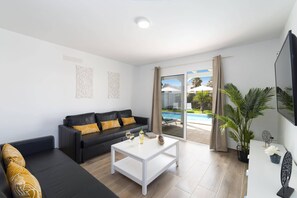 Un salon moderne avec un canapé noir, une table basse blanche et une porte-fenêtre coulissante donnant sur une piscine.