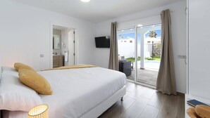 Een slaapkamer met een bed, een televisie en uitzicht op een zwembad en terras.