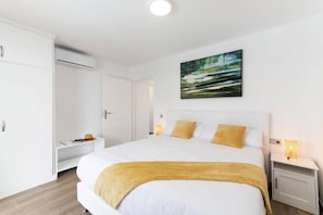 Une chambre avec un grand lit, des murs blancs, un tableau et une armoire.