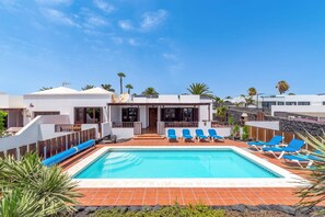 Una piscina con lettini, un edificio bianco con un balcone e un cielo azzurro limpido.