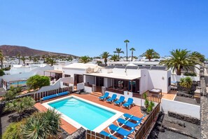 Area piscina su tetto con poltrone relax e una piscina, circondata da edifici bianchi e palme.