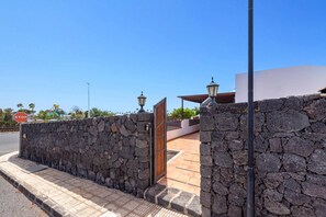 Un muro de piedra con una señal de stop y un portón que da a un edificio con techo de tejas.