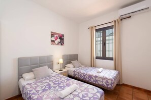 Habitación de hotel con dos camas, una mesita de noche, una lámpara, una ventana con cortinas e un equipo de aire acondicionado instalado en la pared.