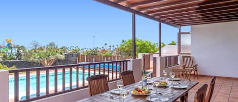 Un espace extérieur aménagé pour prendre les repas, avec vue sur une piscine et un ciel dégagé.
