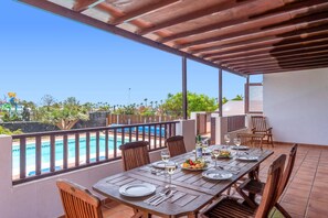 Zona pranzo all'aperto con vista su una piscina e un cielo sereno.