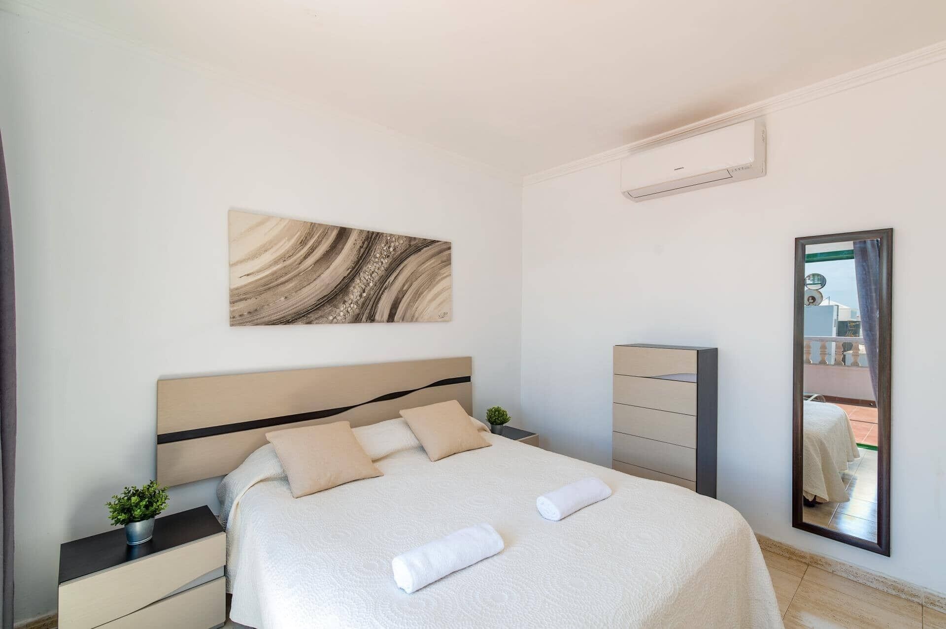 Une chambre d’hôtel comprenant un lit, une table de chevet, une commode, un miroir et un climatiseur fixé au mur.