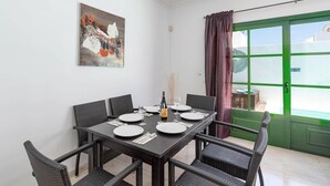 Comedor con una mesa dispuesta para cuatro, sillas de mimbre, un cuadro en la pared y una puerta verde con ventanal.