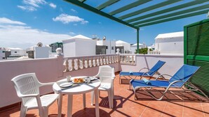 Una terraza en la azotea con sillas blancas, una mesa con desayuno y tumbonas azules.