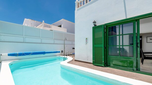 Una piscina con cubierta azul, una puerta verde y un edificio blanco con balcones.