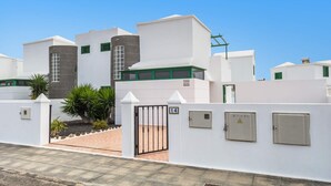 Un edificio moderno con fachada blanca, marcos de ventanas verdes y una entrada protegida por una reja.
