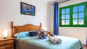 Una cama bien hecha con un cojín celeste y blanco a lunares, un cabecero de madera y una mesita de noche con lámpara.