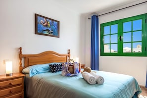 Un lit bien fait, avec un oreiller à pois bleus et blancs, une tête de lit en bois et une table de chevet surmontée d’une lampe.