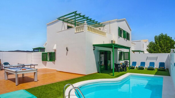 Zona junto a la piscina con piscina, mesa y sillas.