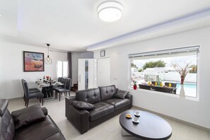 Ein modernes Wohnzimmer mit Ledersofa, einem Essbereich mit Tisch und Stühlen sowie einem großen Fenster mit Blick ins Freie.