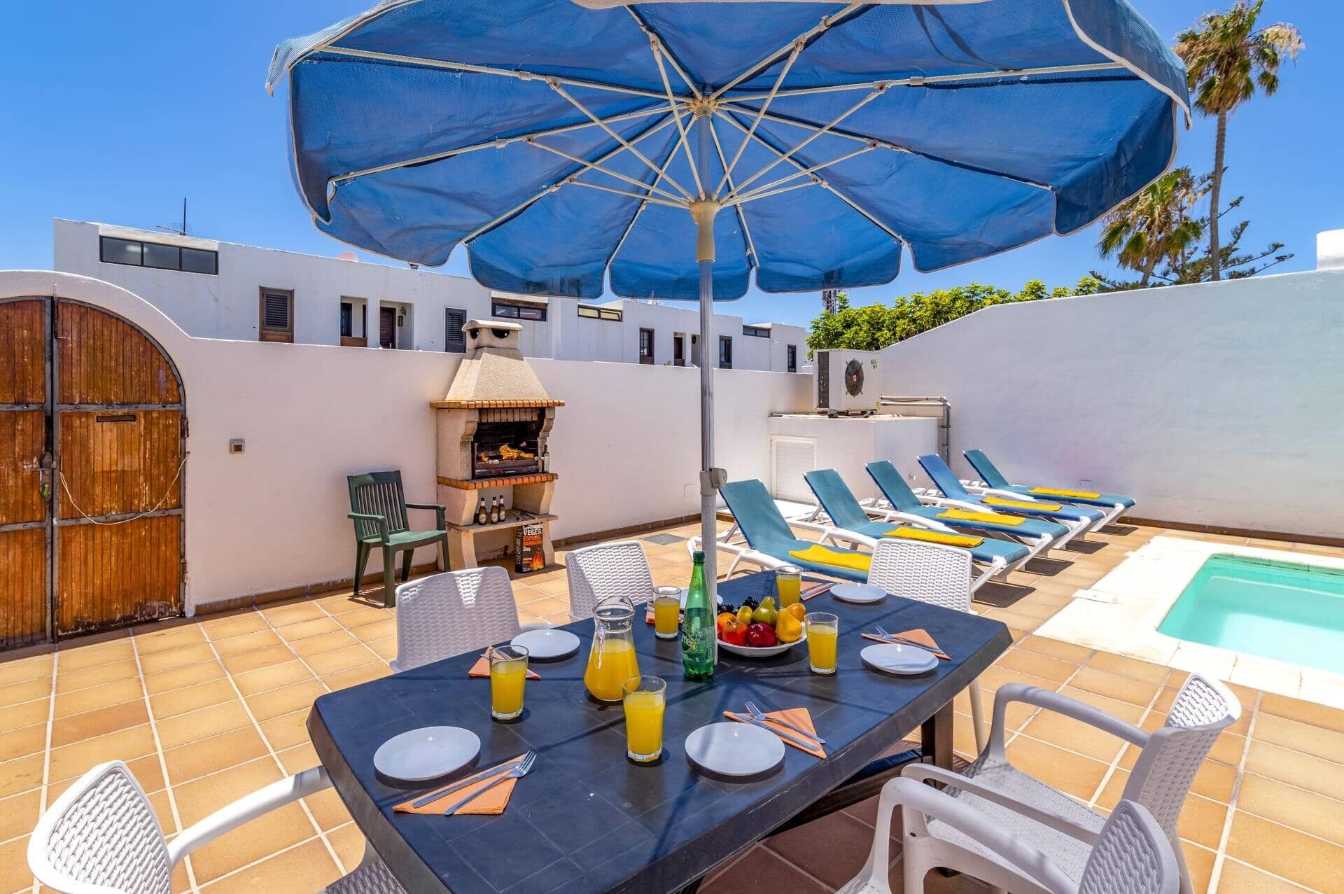 A patio with a table set for dining, a grill, and lounge chairs by a pool.