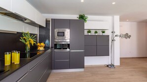 Eine moderne Küche mit grauen Schränken, einem eingebauten Backofen und einer Mikrowelle. Es gibt eine schwarze Arbeitsplatte mit einer Vase gelber Blumen und Gläsern Orangensaft.