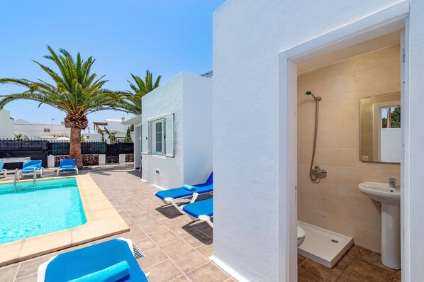 A pool area with lounge chairs, a shower, and a bathroom with a sink and toilet.