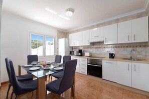 A modern kitchen with white cabinets, a glass dining table, and a view of the outdoors.