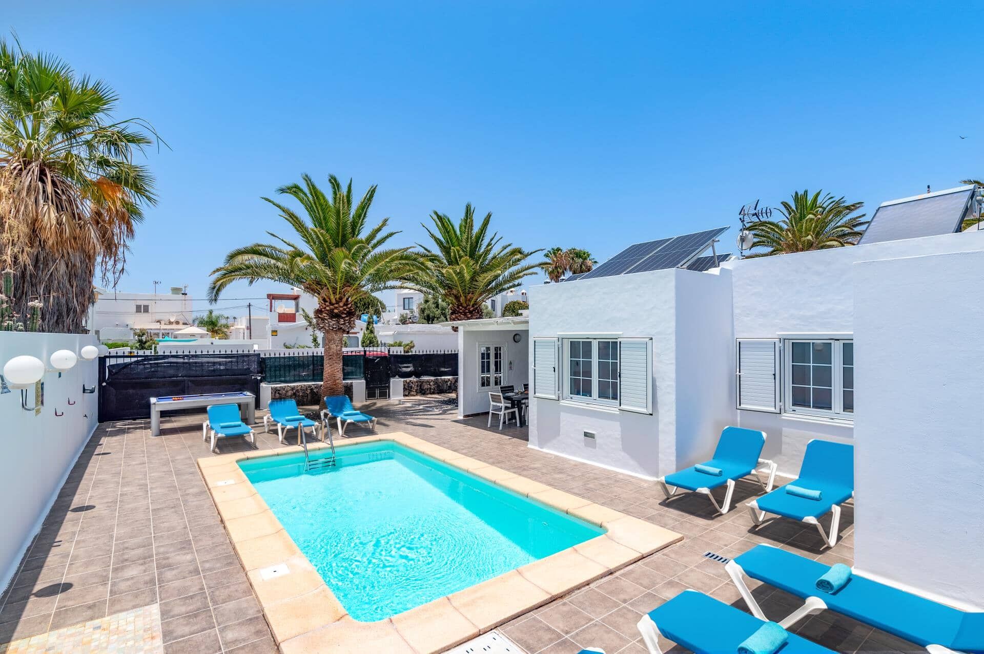 A swimming pool with lounge chairs, a covered seating area, and a white building with windows.