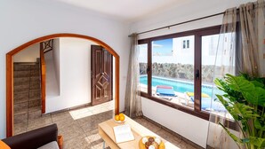 Habitación con vista a una piscina, una puerta de madera, una escalera y una mesa con un libro y naranjas.