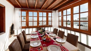 Comedor con techo de madera, ventanas amplias y una mesa dispuesta para seis personas, con platos, vasos y una botella de vino.
