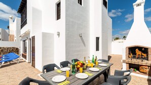 Un área de comedor al aire libre con una mesa larga dispuesta para cuatro personas, rodeada de muros de piedra y una parrilla.