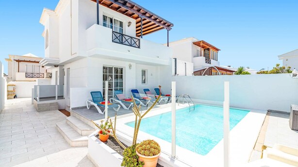 Ett tvåvåningshus med en swimmingpool, utomhusmöbler och en trädgård.