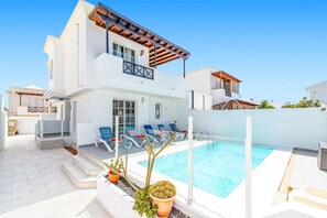 Une maison à deux étages avec une piscine, un espace salon extérieur et un jardin.
