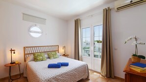 A bedroom with a bed, a bedside table, a lamp, a window, and an air conditioning unit. - Villa Laurona by Villa Plus (Puerto del Carmen)