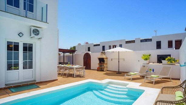 A pool area with a clear blue pool, white walls, and a pergola. - Villa Laurona by Villa Plus (Puerto del Carmen)