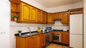 A kitchen with wooden cabinets, a stainless steel sink, a microwave, a toaster, and a refrigerator. - Villa Laurona by Villa Plus (Puerto del Carmen)