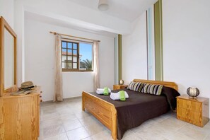 Une chambre à coucher avec un lit en bois, une table de chevet, une commode, un miroir et une fenêtre avec des rideaux.