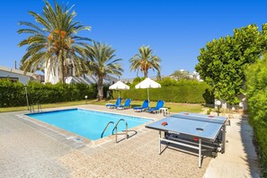 A swimming pool with lounge chairs and a ping pong table.