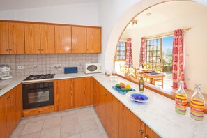 A kitchen with wooden cabinets, a stove, a microwave, and a window overlooking a dining area with a table and chairs.